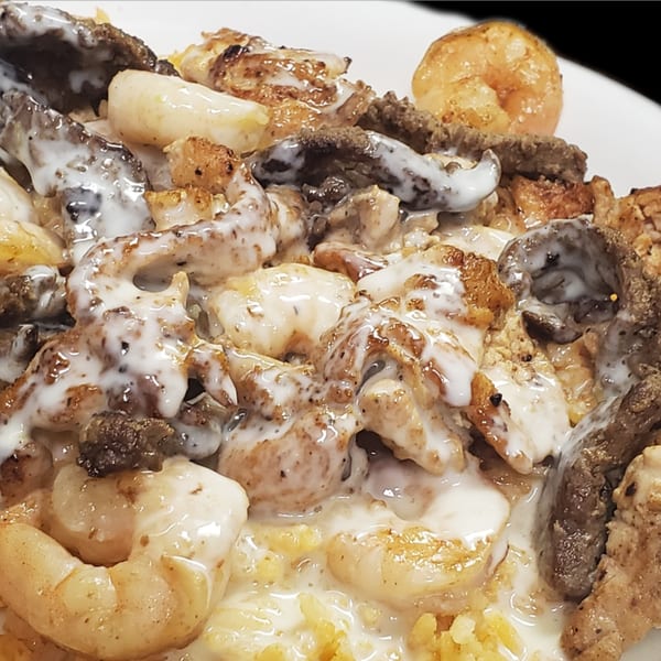 Close-up of a Mexican dish with shrimp, steak, chicken, and rice, all covered in a creamy white sauce.