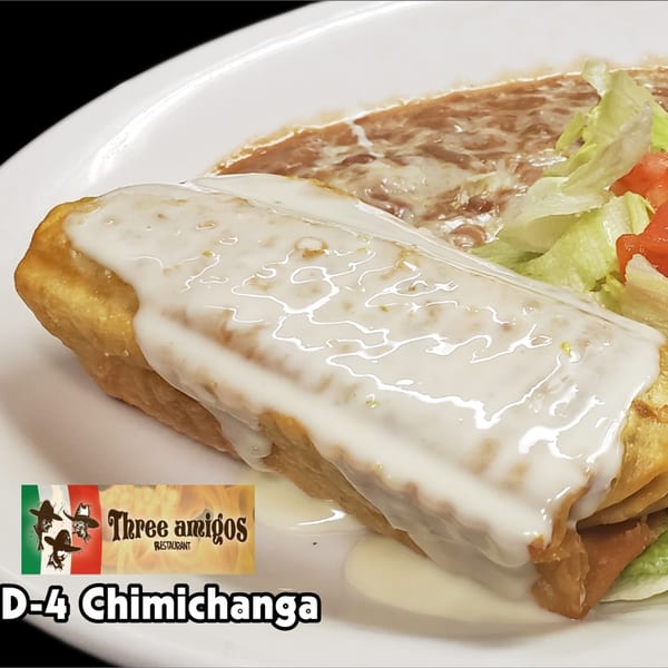 A golden-brown chimichanga topped with white sauce, served with refried beans, lettuce, and diced tomatoes.